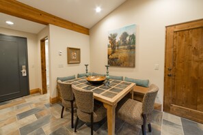 Een eetruimte met een houten tafel en gestreept beklede stoelen, een schilderij aan de muur en een deur met houten omlijsting.