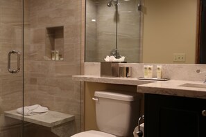 Een moderne badkamer met een glazen douchecabine, een marmeren aanrechtblad en een toilet.