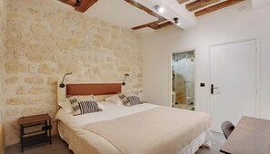 Une chambre avec un mur en pierre, un lit avec des coussins à rayures, une table de chevet et une porte avec un panneau de verre.