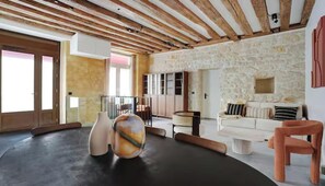Une pièce avec un mur en pierre, un canapé blanc, un plafond en bois et une grande fenêtre.