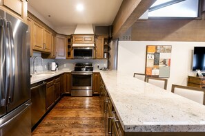 A modern kitchen with stainless steel appliances, wooden cabinets, and a marble countertop. - NEW! Bald Eagle Two Bedroom (Park City)