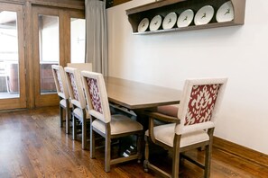 A dining area with a wooden table and four chairs, a shelf with plates, and a view through a glass door. - NEW! Bald Eagle Two Bedroom (Park City)