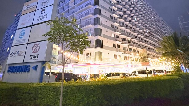 A multi-story hotel with a modern design, featuring balconies on each floor, a visible parking area, and various commercial signs on the facade. - Hotel Comfort at Shell MOA - Near SMX & IKEA (Pasay City)