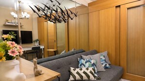 A modern living room with a grey sofa, decorative pillows, a wooden side table, and a hanging light fixture. - Hotel Comfort at Shell MOA - Near SMX & IKEA (Pasay City)