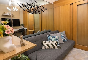 Ein modernes Wohnzimmer mit einem grauen Sofa, dekorativen Kissen, einem Holztisch und einer Pendelleuchte.
