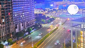 A multi-level building with a modern design, a busy road with vehicles, and a large illuminated structure in the background. - Hotel Comfort at Shell MOA - Near SMX & IKEA (Pasay City)