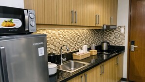 A modern kitchen with wooden cabinets, a stainless steel refrigerator, a microwave, a sink, and a tiled backsplash. - Hotel Comfort at Shell MOA - Near SMX & IKEA (Pasay City)