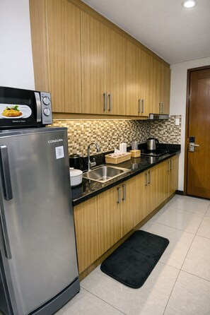 Eine moderne Küche mit Holzschränken, einem Edelstahlkühlschrank, einer Mikrowelle, einem Spülbecken und einer gefliesten Spritzschutzwand.