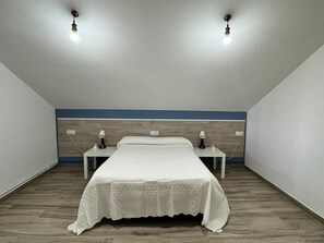 Une chambre Ă coucher avec un lit, deux tables de chevet, une commode, un plancher en bois et un mur dâaccent bleu.