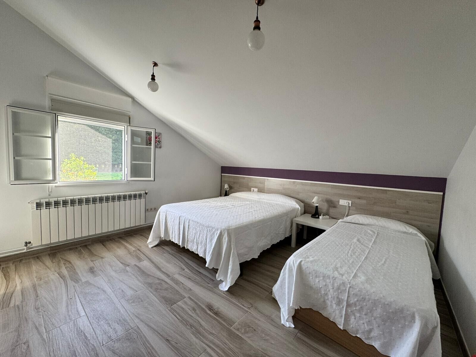 Een slaapkamer met twee bedden, een raam, een radiator en een plafondlamp.