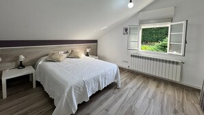 A bedroom with a bed, bedside tables, a window with an open view, a radiator, and a ceiling light. - Apartment at Casa Rural La Pradera with Mountain Views, Garden, and Wi-Fi (A Espiñeira)