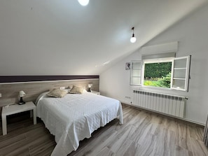 Un dormitorio con cama, mesitas de noche, ventana con vista despejada, radiador e iluminación en el techo.