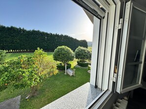 Une vue depuis une fenĂȘtre donnant sur un jardin bien entretenu, avec des haies taillĂ©es avec soin et une pelouse impeccable.