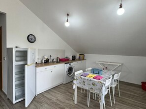 A compact kitchen with a washing machine, a dining table with chairs, and a clock on the wall.
