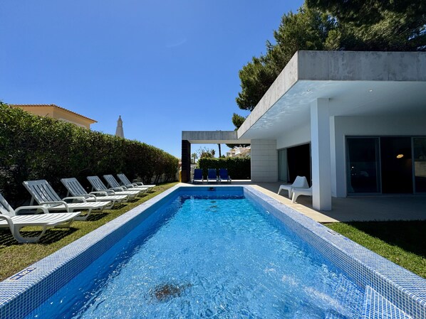 Ein moderner Poolbereich mit Liegestühlen, einem klaren, blauen Pool und einem Gebäude mit großen Fenstern.