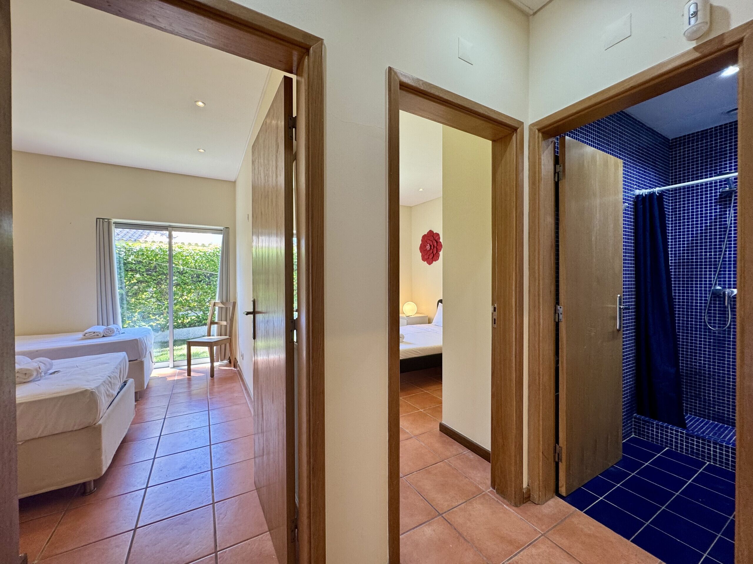 Une chambre d’hôtel avec un lit, une chaise, une fenêtre donnant sur un beau paysage et une salle de bain carrelée de bleu.