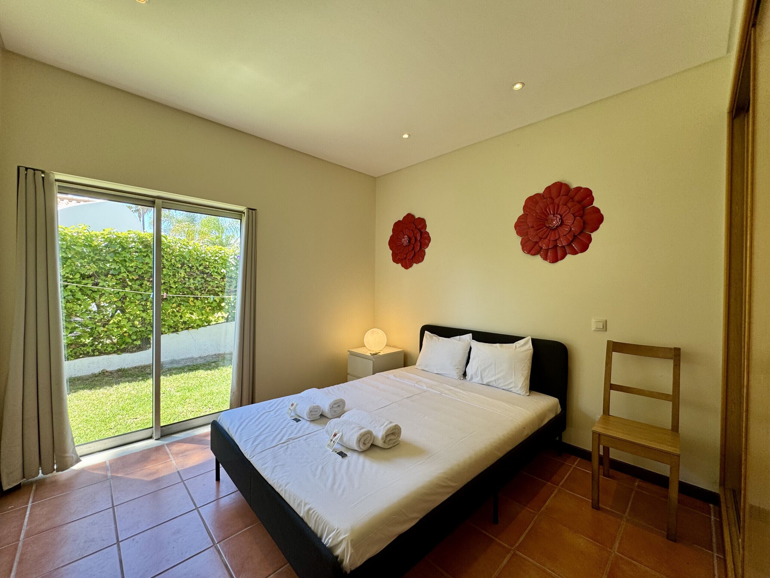 Une chambre d’hôtel avec un lit, une chaise, une table de chevet et une vue sur la verdure, visible à travers une porte coulissante.