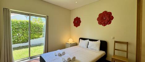Une chambre d’hôtel avec un lit, une chaise, une table de chevet et une vue sur la verdure, visible à travers une porte coulissante.