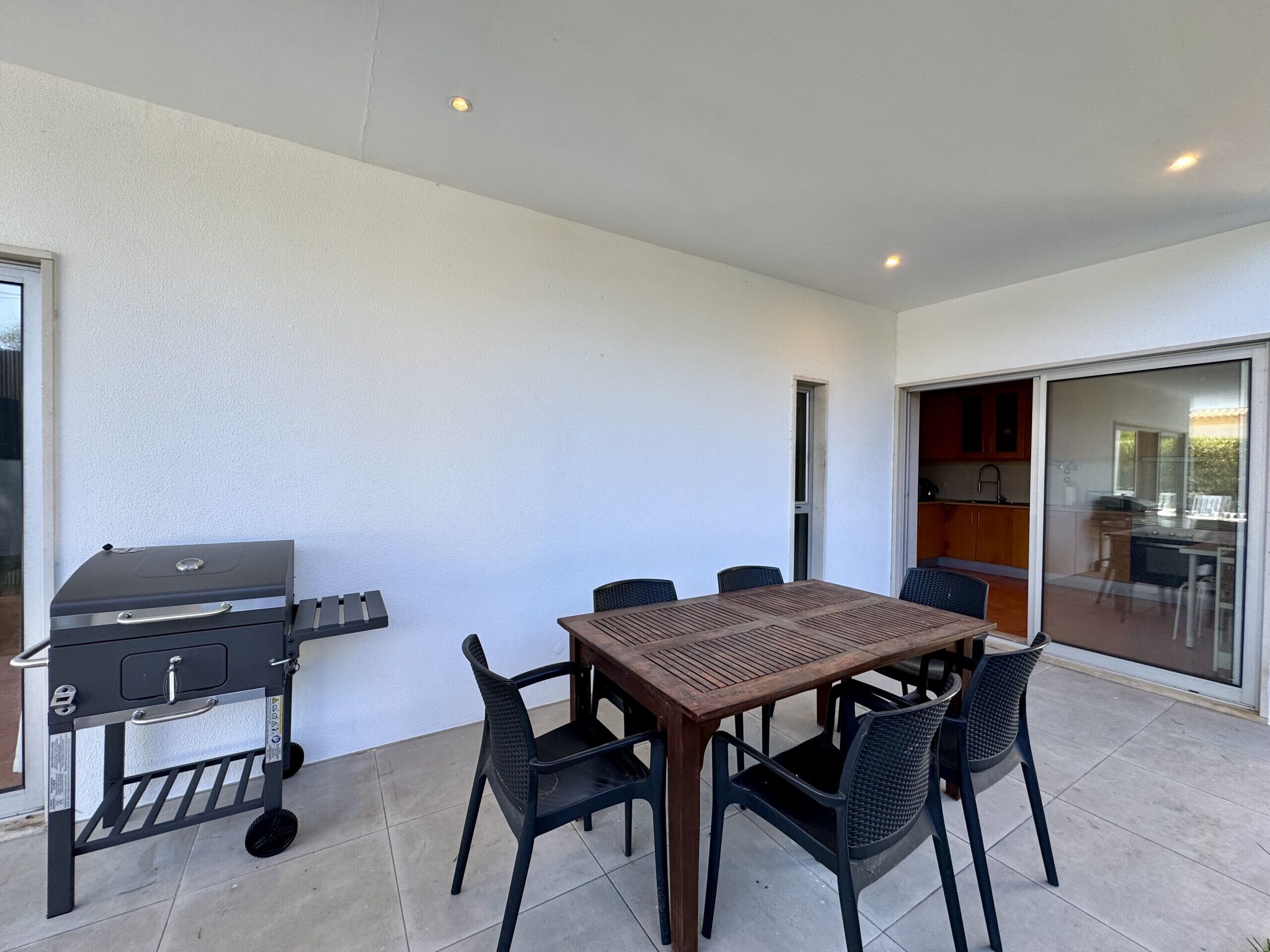 Une terrasse extérieure avec un barbecue, une table en bois et des chaises.