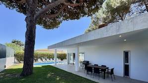 A modern outdoor patio with a pool, a dining area, and a large tree. - Albufeira Balaia Villa 2 by Homing (Albufeira)
