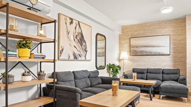 Un salón moderno con dos sofás grises, una mesa de centro de madera y una estantería con adornos.