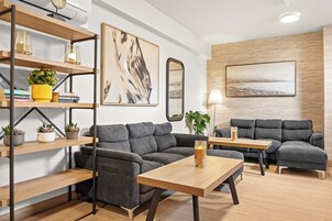 Un salón moderno con dos sofás grises, una mesa de centro de madera y una estantería con adornos.