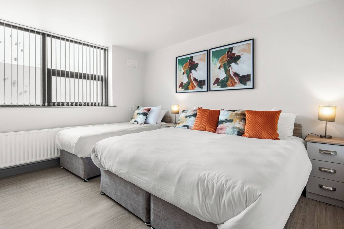 Une chambre d’hôtel moderne avec un grand lit, deux tables de chevet, un radiateur et des œuvres d’art accrochées au mur.