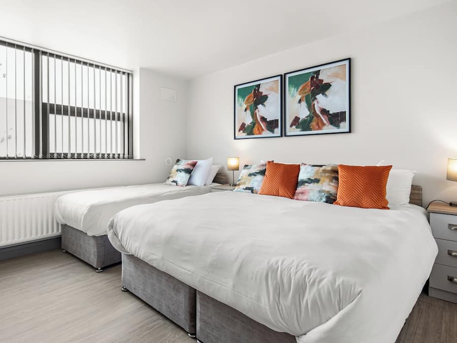 A modern hotel room with a large bed, two bedside tables, a radiator, and artwork on the wall.