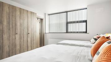 Un dormitorio con un armario de madera, una ventana con persianas, una cama con ropa de cama blanca y un radiador.