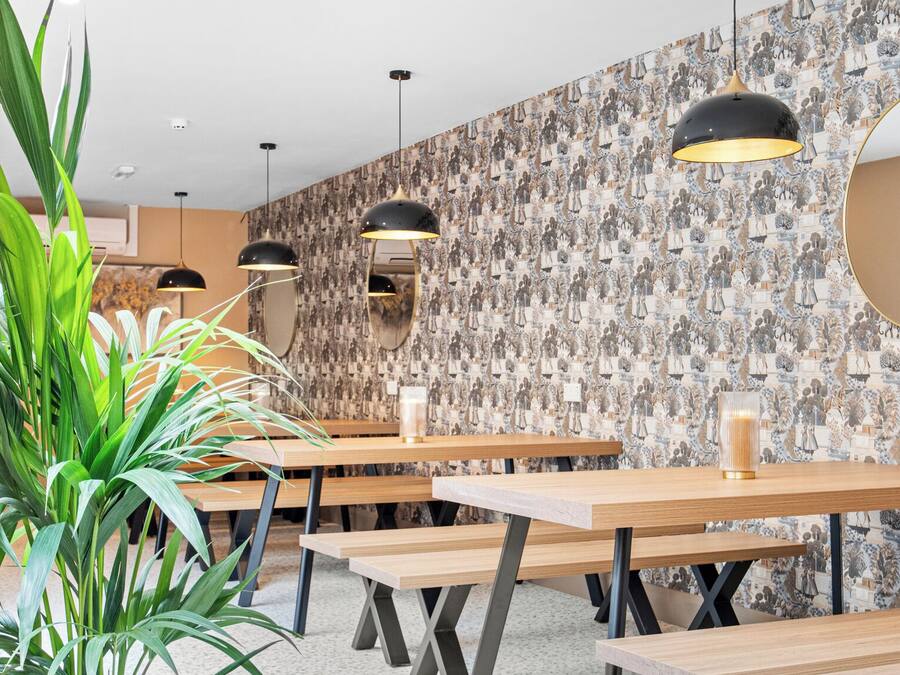 Un comedor moderno con mesas de madera, lámparas colgantes negras y un papel tapiz estampado.