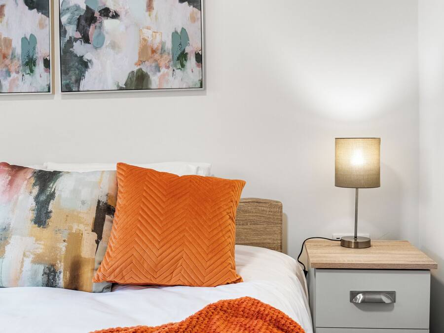 A bedroom with a bed, two pillows, a bedside table with a lamp, and abstract artwork on the wall.