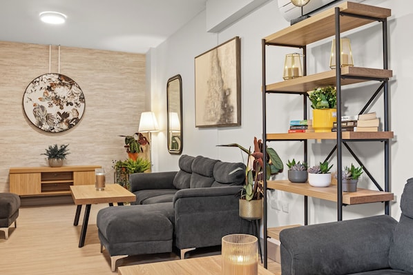 Un salon moderne avec un canapé gris, une table basse en bois et une bibliothÚque remplie de livres et de plantes.