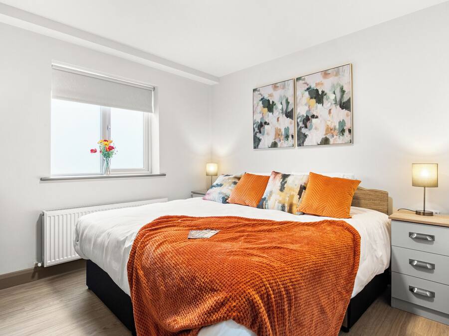 Un dormitorio con cama, mesitas de noche, radiador, ventana con vistas y arte abstracto en la pared.