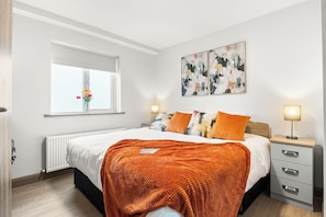 A bedroom with a bed, bedside tables, a radiator, a window with a view, and abstract wall art.
