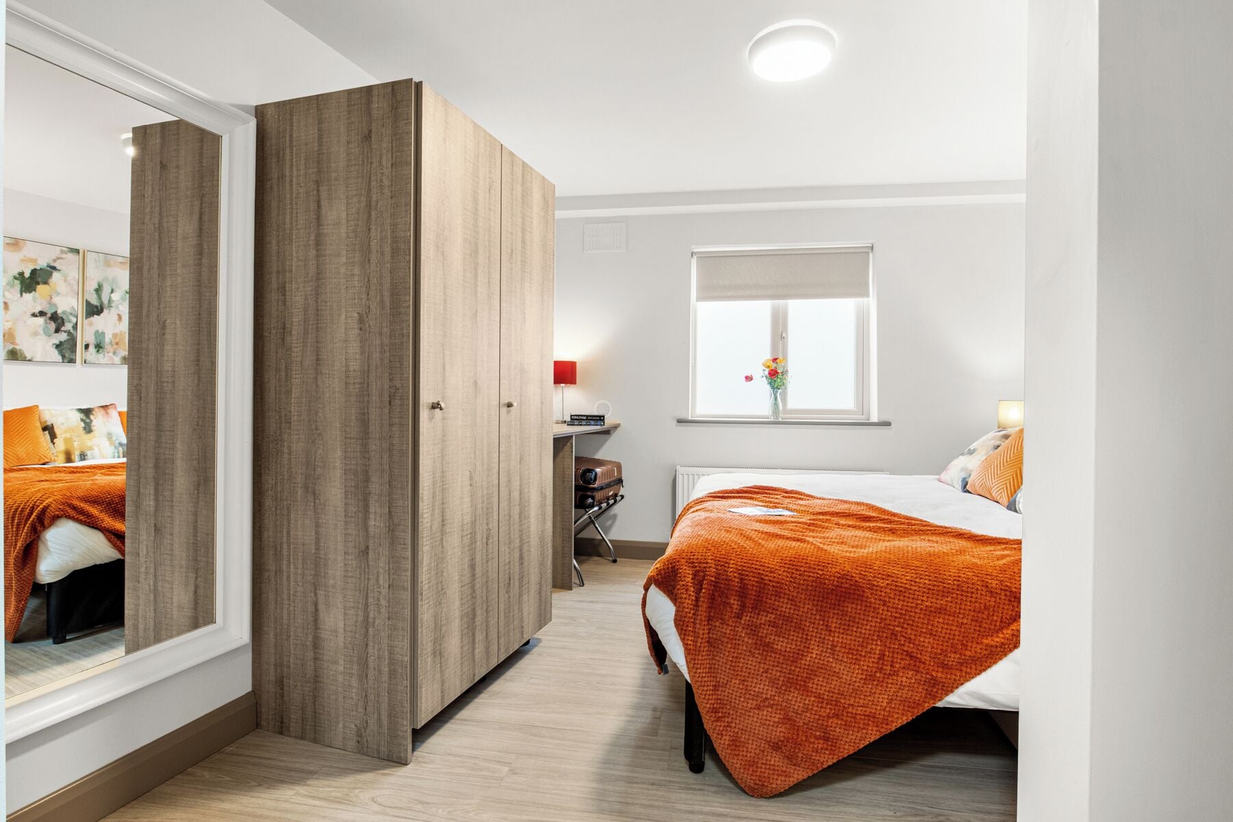 Un dormitorio con cama, armario, ventana y mesita de noche.