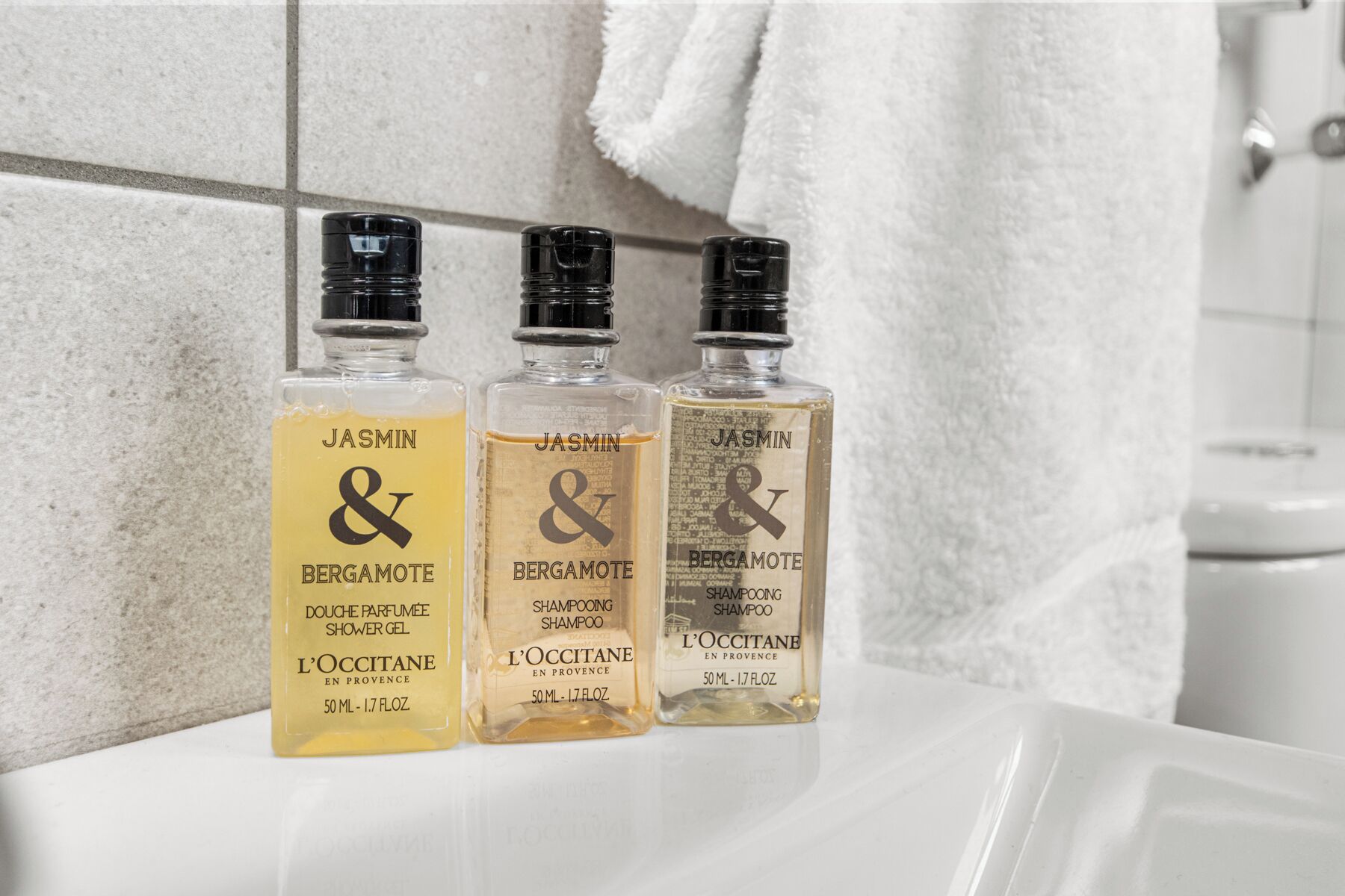 Three bottles of JASMIN & BERGAMOTE shampoo on a bathroom counter.