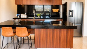 A modern kitchen with wooden cabinets, a stainless steel refrigerator, a built-in oven, and a large island with bar stools. - Condo with excellent views 10 minutes from the boardwalk Super equipped (Puerto Vallarta)