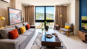 A modern living room with a sofa, armchair, coffee table, and a large window with a view. - Condo with excellent views 10 minutes from the boardwalk Super equipped (Puerto Vallarta)