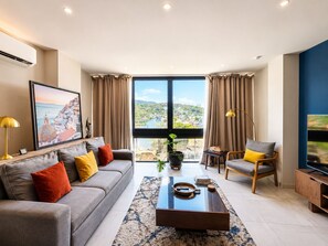 Ein modernes Wohnzimmer mit Sofa, Sessel, Couchtisch und einem großen Fenster mit Blick.