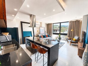 Eine moderne Küche mit einer zentralen Kochinsel, einem Essbereich mit einer Couch und einem großen Fenster mit Blick.