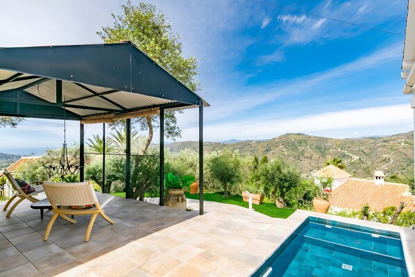 Ein Poolbereich mit einer Pergola, Liegestühlen und Blick auf die Landschaft.