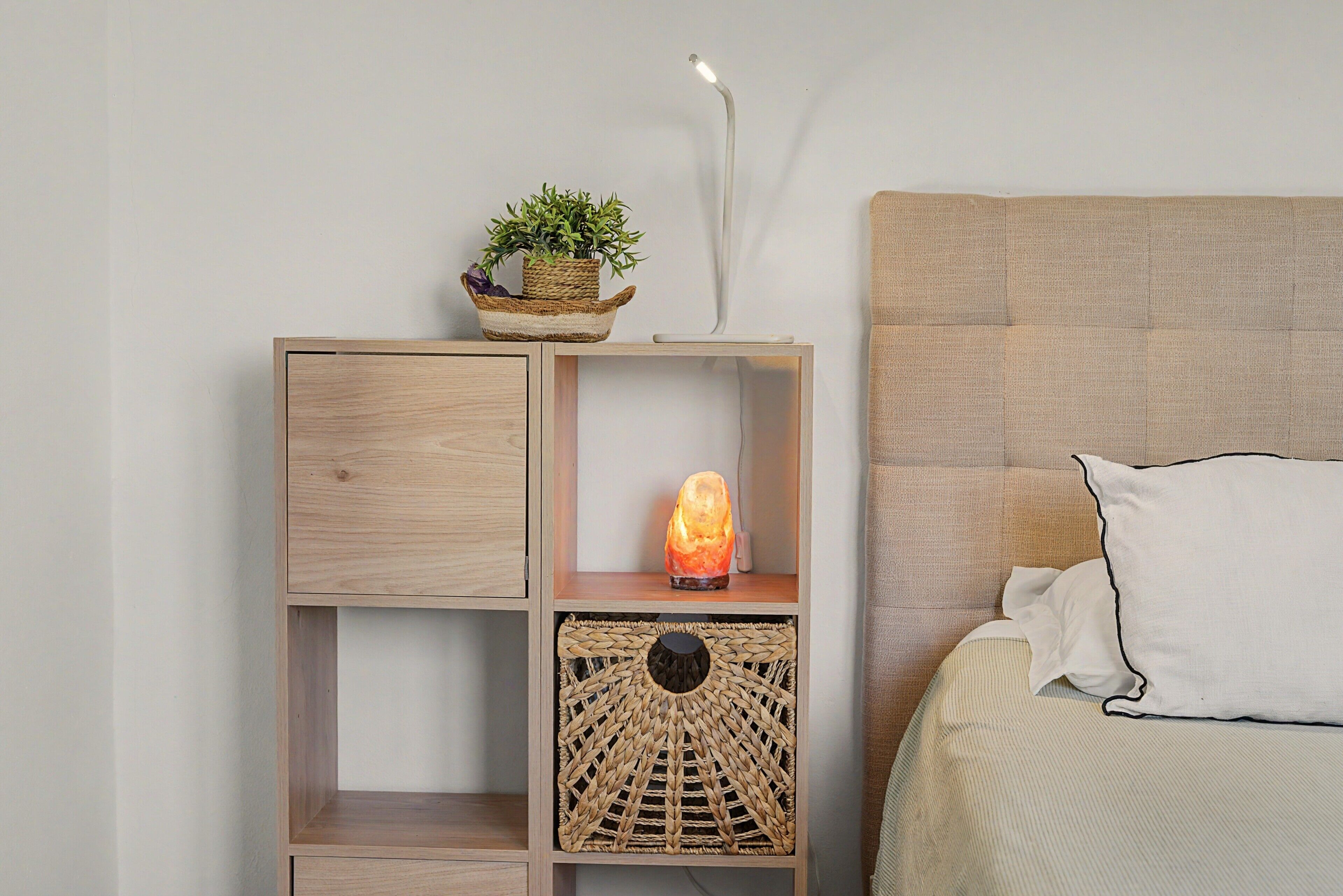 Een houten nachtkastje met een gevlochten mand, een verwarmde steen en een potplant.