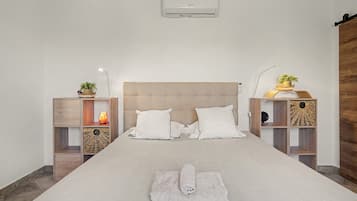Une chambre moderne avec un grand lit, deux tables de chevet, un climatiseur fixé au mur et un plancher en bois.