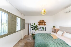 Een slaapkamer met een bed, een kamerplant, een houten kast en een kroonluchter.