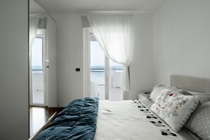 Ein Schlafzimmer mit Bett, Nachttisch, einem Fenster mit Vorhängen und Blick auf das Meer.