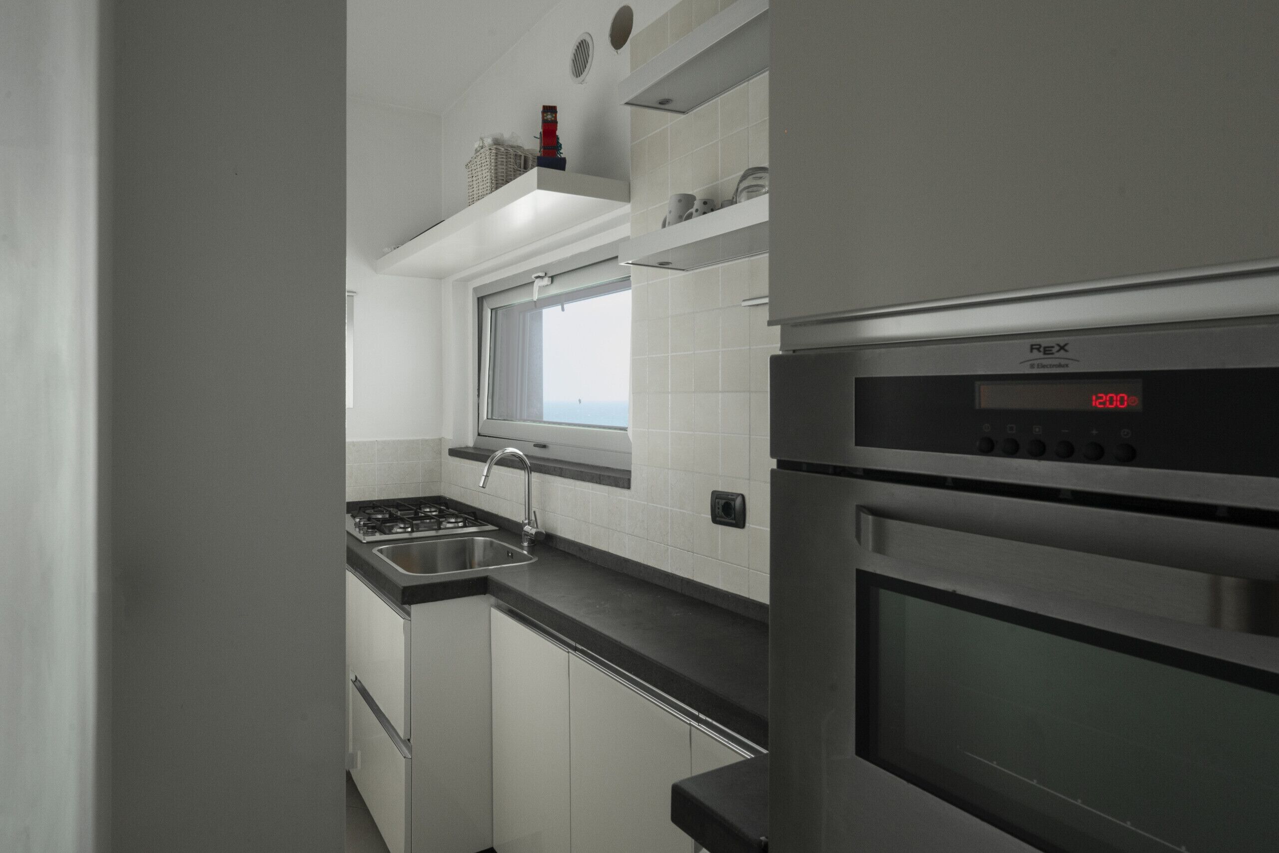 Een moderne keuken met witte kastjes, een roestvrijstalen fornuis, een inbouwoven en een raam boven de gootsteen.