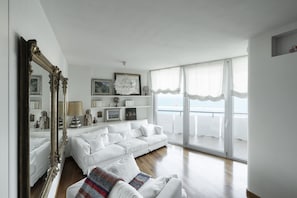 A spacious living room with a white sofa, a large mirror, and a balcony with a view.