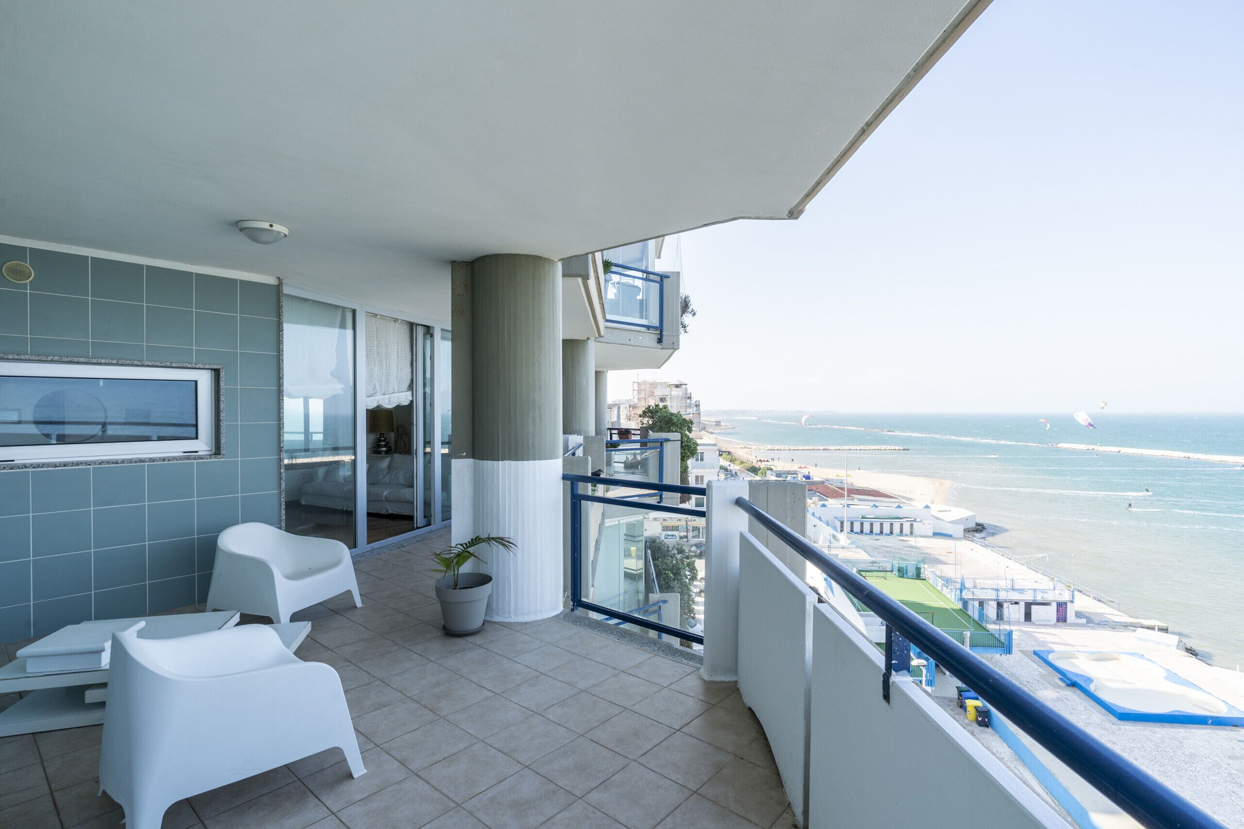 A balcony with a view of the sea, a TV, and a seating area with a plant.