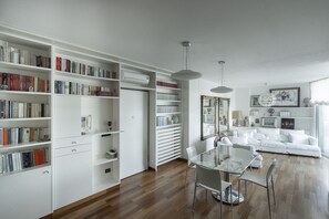 Ein modernes Wohnzimmer mit einem weißen Sofa, einem Glastisch und einem Bücherregal voller Bücher.