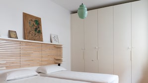 Une chambre avec deux lits, une tête de lit en lattes de bois, une suspension verte et une grande armoire.